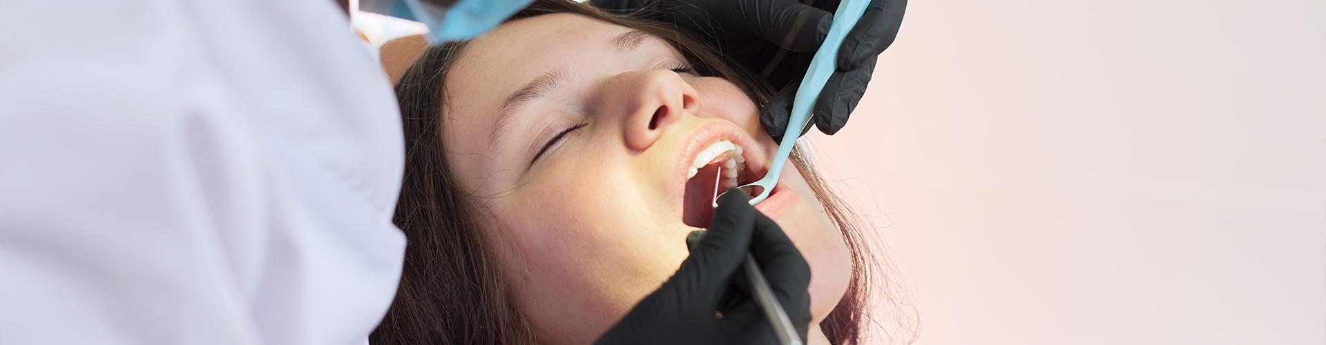 Dentist using dental tool in sleeping patient's mouth.